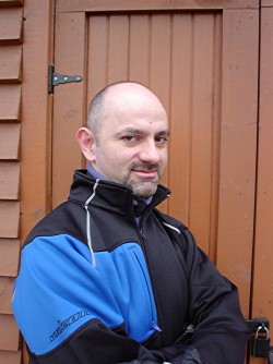 Me in black jacket with blue patch, photographed against brown door
